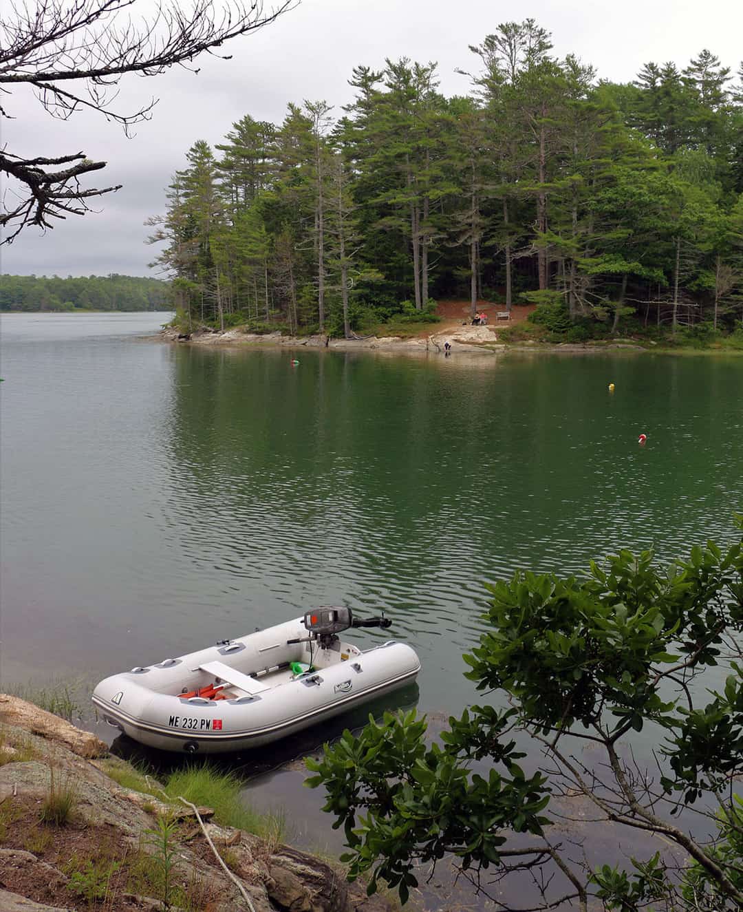 Inflatable dinghy tied to near shore; opposite shore has rocky ledge and tall firs.