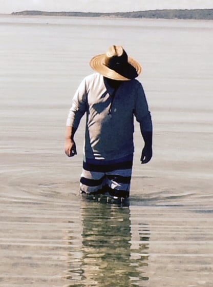 man wading in water, looking for oysters