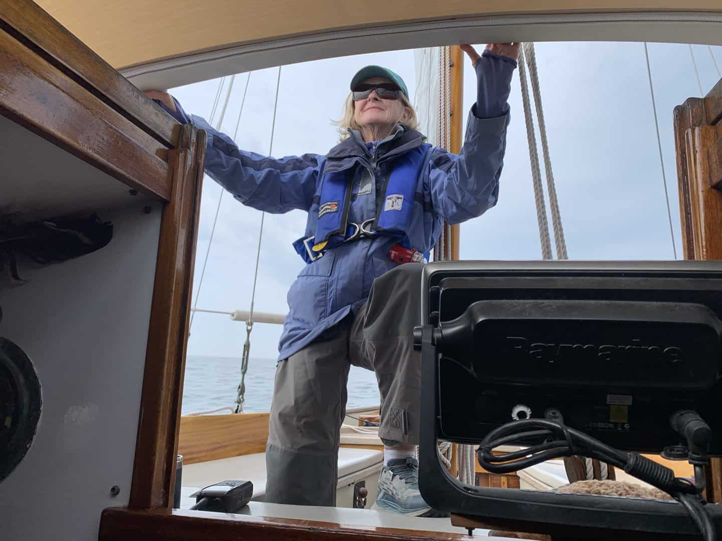 Woman standing in cockpit of sailboat, watching over cabin top.