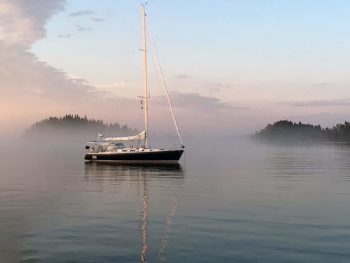 Dark blue sailboat at anchor with fog creeping in.