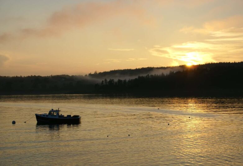 Golden sunset over Bartlett Island, with lobster boat moored in foreground on very still water.