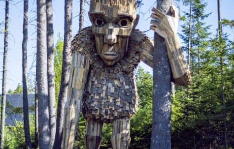 Large wooden troll statue with arm wrapped around tree.