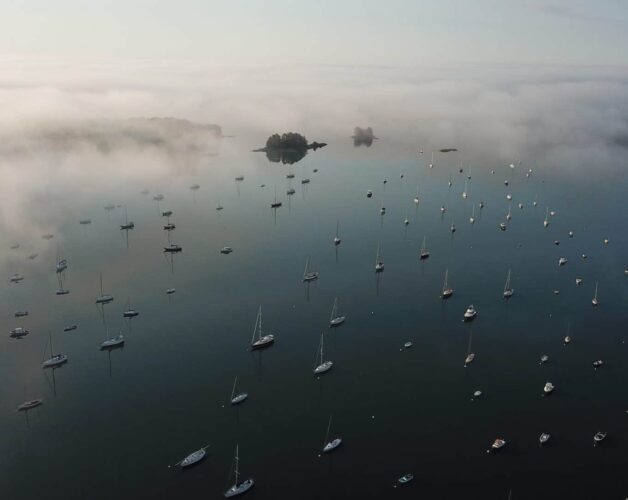 Aerial view of Harraseeket River with many boats moored and fog creeping in.