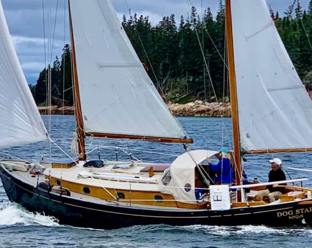 S/V Dog Star, a black ketch, sailing along a Maine shore.