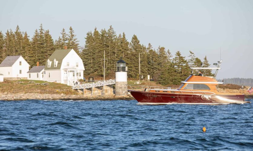 burgundy powerboat in front of lighthouse