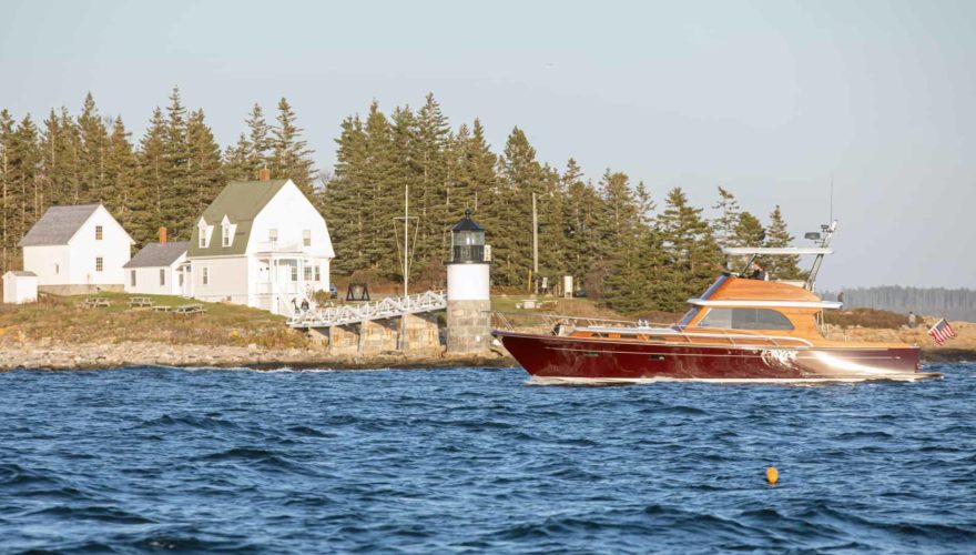 burgundy powerboat in front of lighthouse