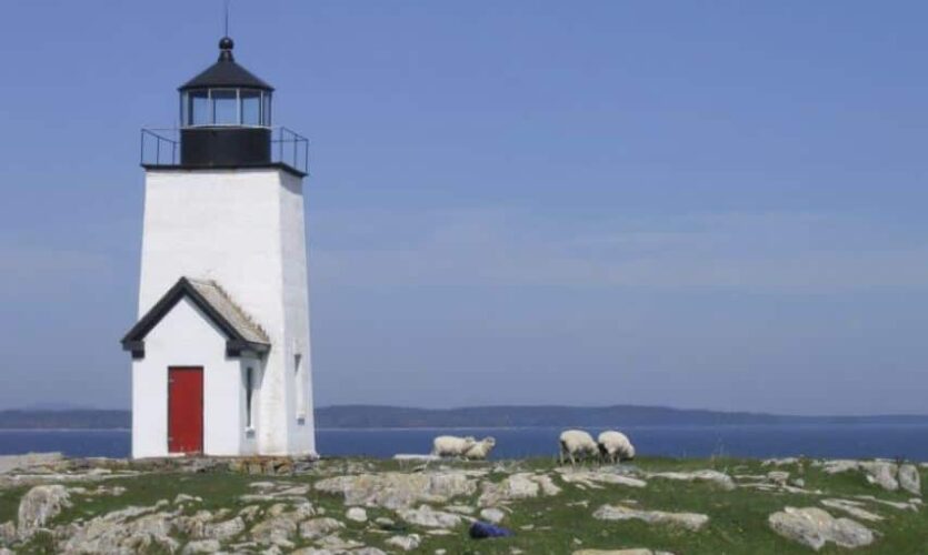 Sqare white lighthouse tower on a rocky knoll overlooking the ocean.