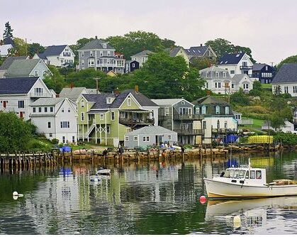 Many buildings stretching from the water's edge to the top of a hill with a lobster boat moored in the foreground.