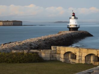 Sparkplug lighthouse at the end of a long stone pier.