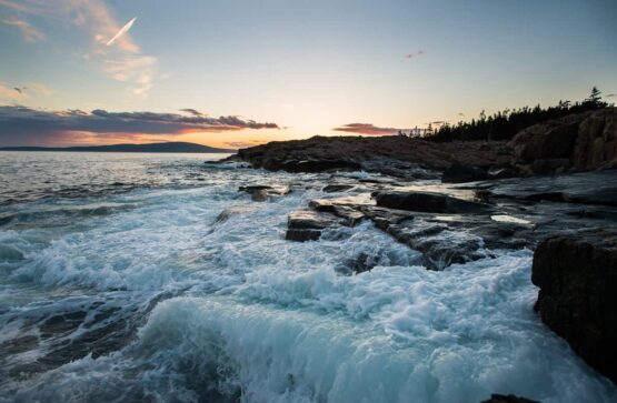 Rocky shoreline with foaming water pouring over the rocks and the sunsset beyond.