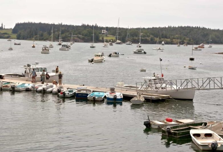 Dock with dinghies on one side and a lobster boat on the other; boats are moored in the background.