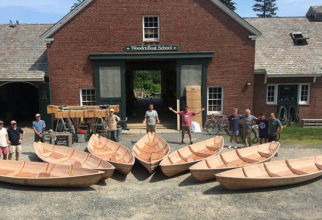 People standing outside the Wooden Boat School building with six newly-built wooden boats.