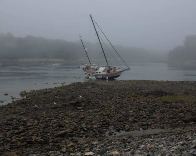 A sailboat aground at low tide in the York Harbor entrance.